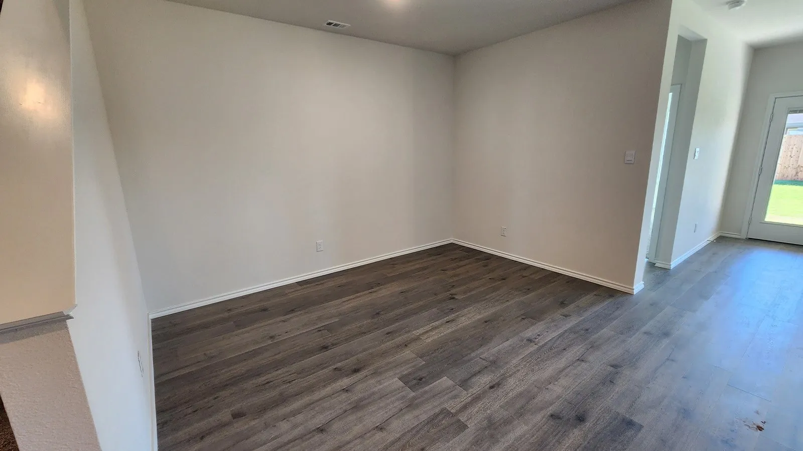 Spacious interior featuring wood-finish flooring, light-toned walls, white trim, and a rear door with an exterior view