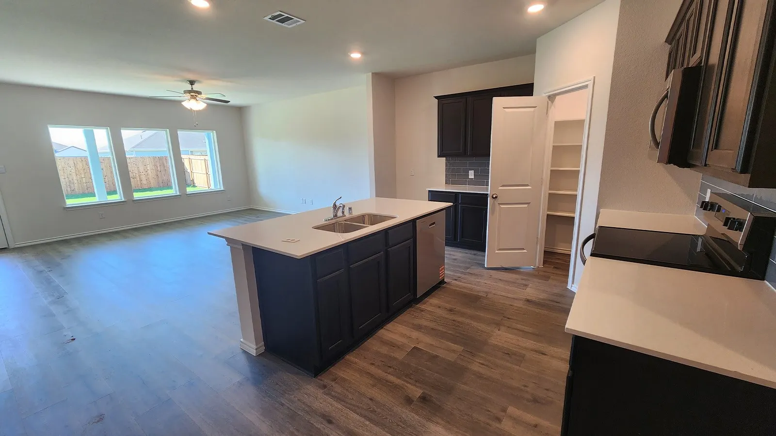 Open-concept living space featuring wood-finish flooring, a kitchen island with dual sinks and a dishwasher, dark cabinetry, and light countertops