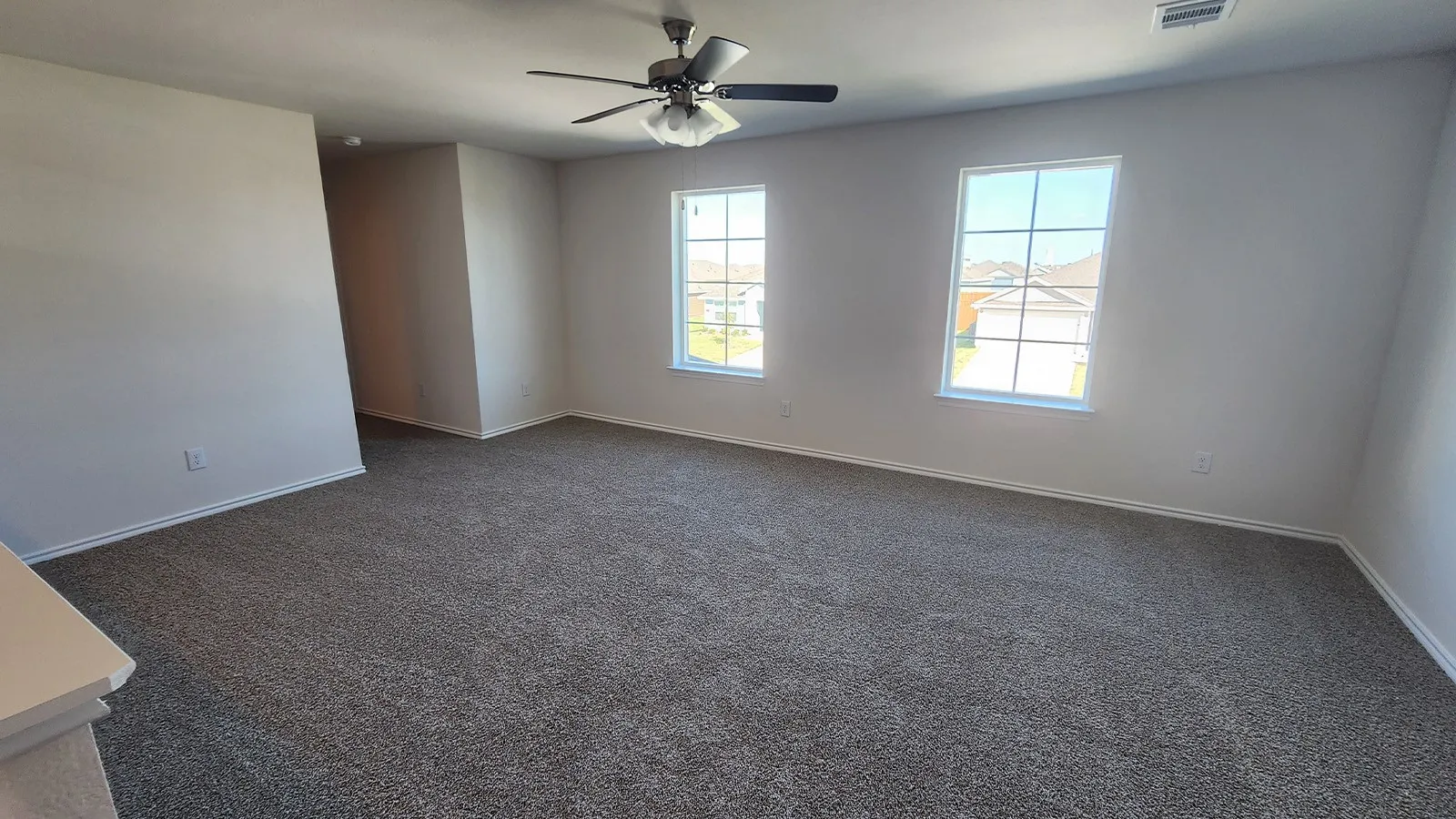 Carpeted interior space featuring two windows with grid patterns, a ceiling fan with integrated lighting, and neutral wall tones