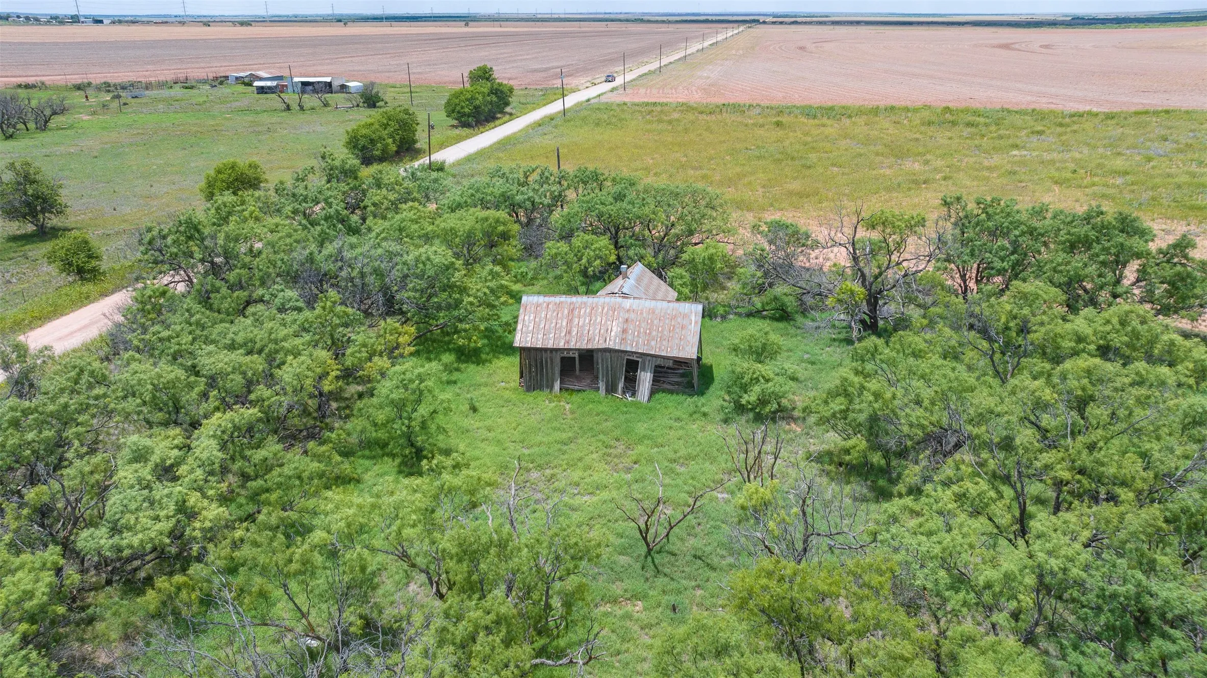 Rural property featuring an existing structure with a metal roof, surrounded by mature trees and open fields