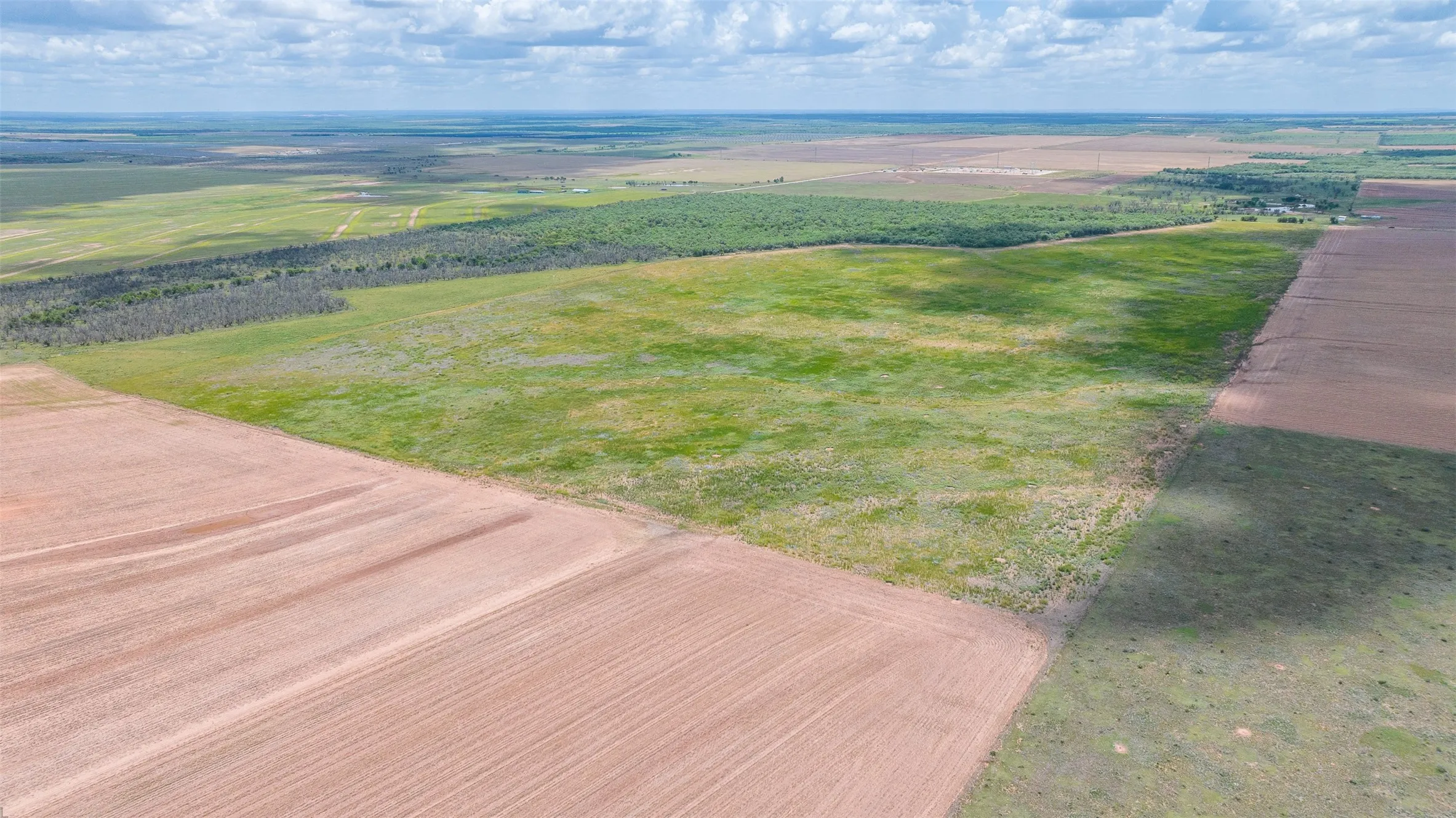 Expansive rural acreage featuring cultivated fields, natural grasslands, and distant tree lines under an open sky