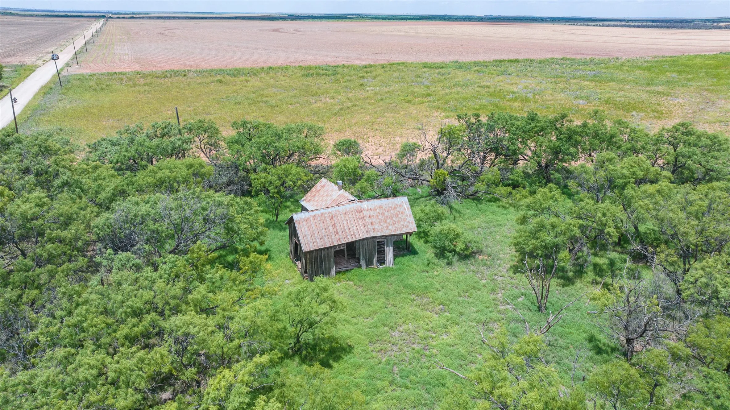 Rural acreage featuring a wooden structure with a corrugated metal roof, surrounded by mature trees and expansive grassy areas