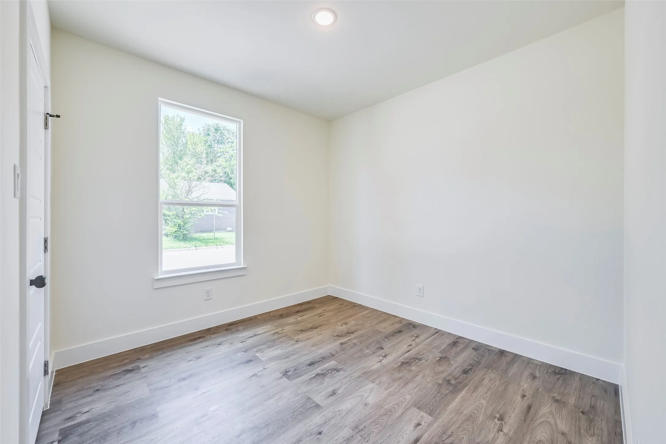 Room featuring wood-finish flooring, a single window with white trim, and a recessed ceiling light