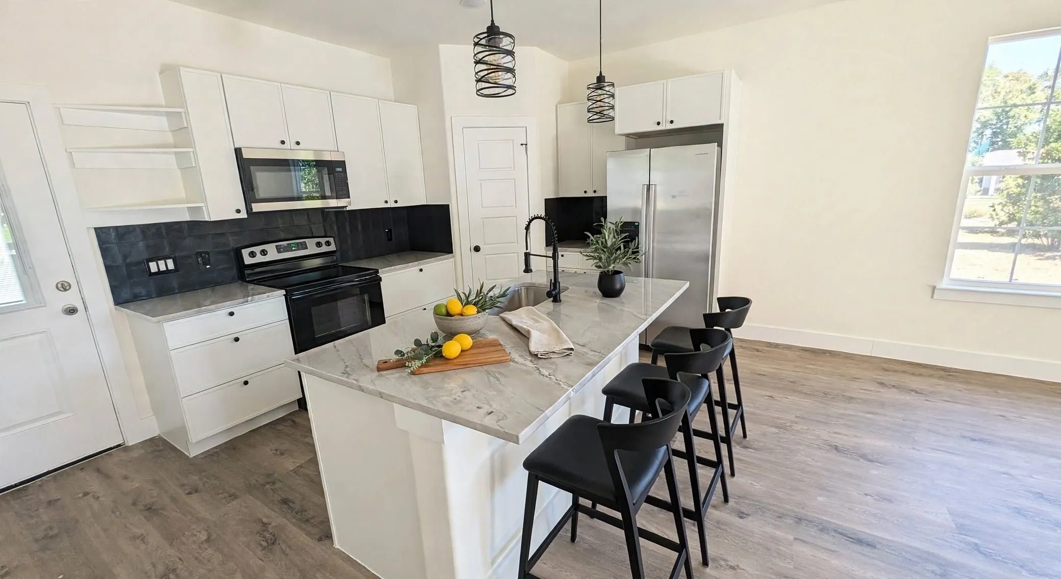 Contemporary kitchen featuring a white island with a light-toned countertop, stainless steel appliances, dark tile backsplash, and wood-finish flooring