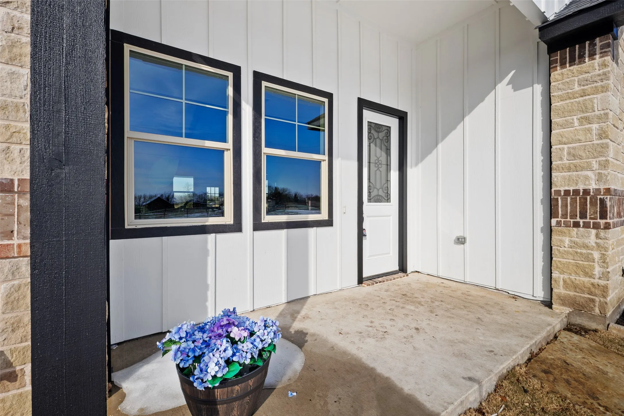 Exterior featuring board and batten siding, stone facade, black trim windows, a decorative glass entry door, and a concrete porch