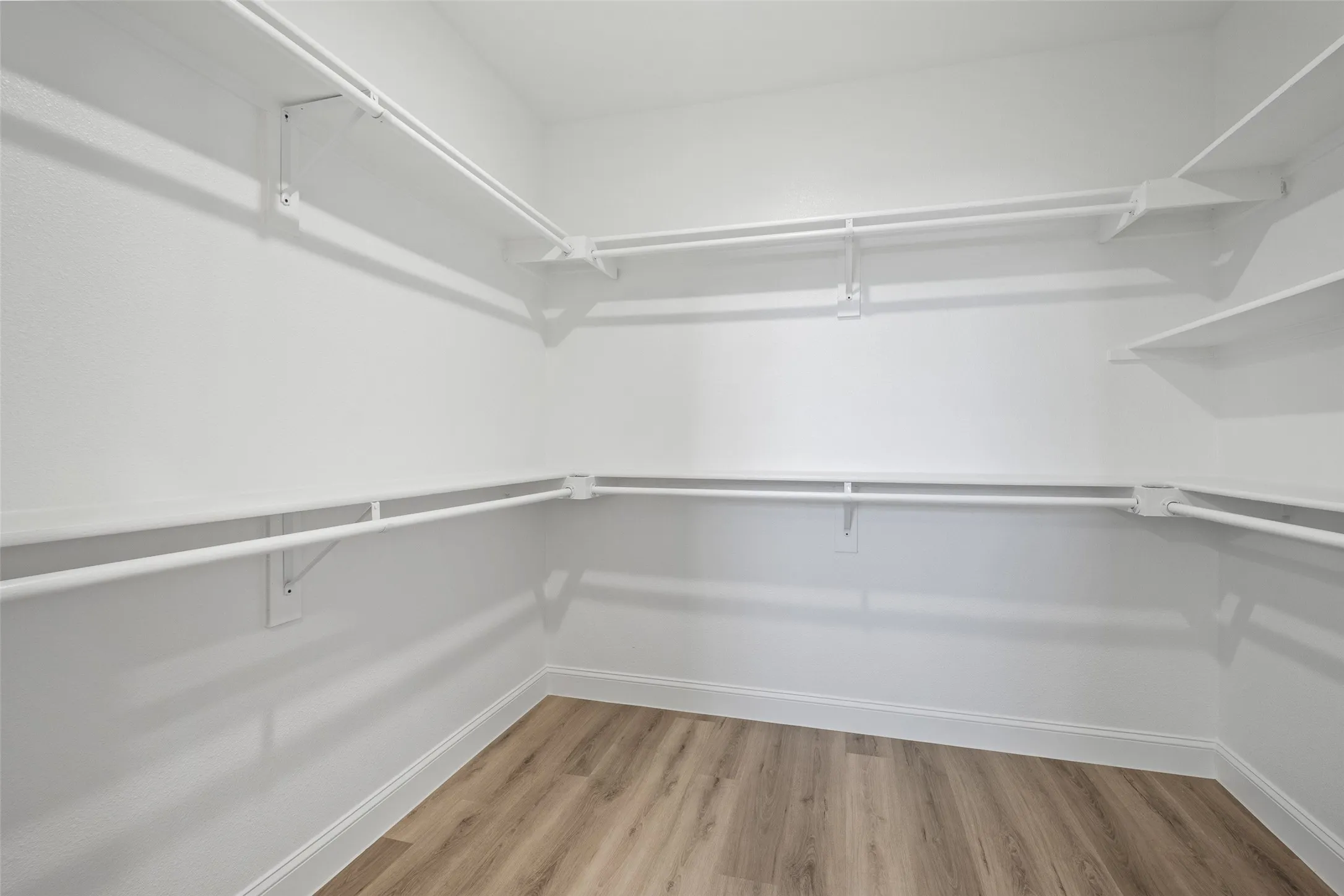 Spacious walk-in closet featuring white wire shelving, multiple hanging rods, corner shelving units, and wood-finish flooring