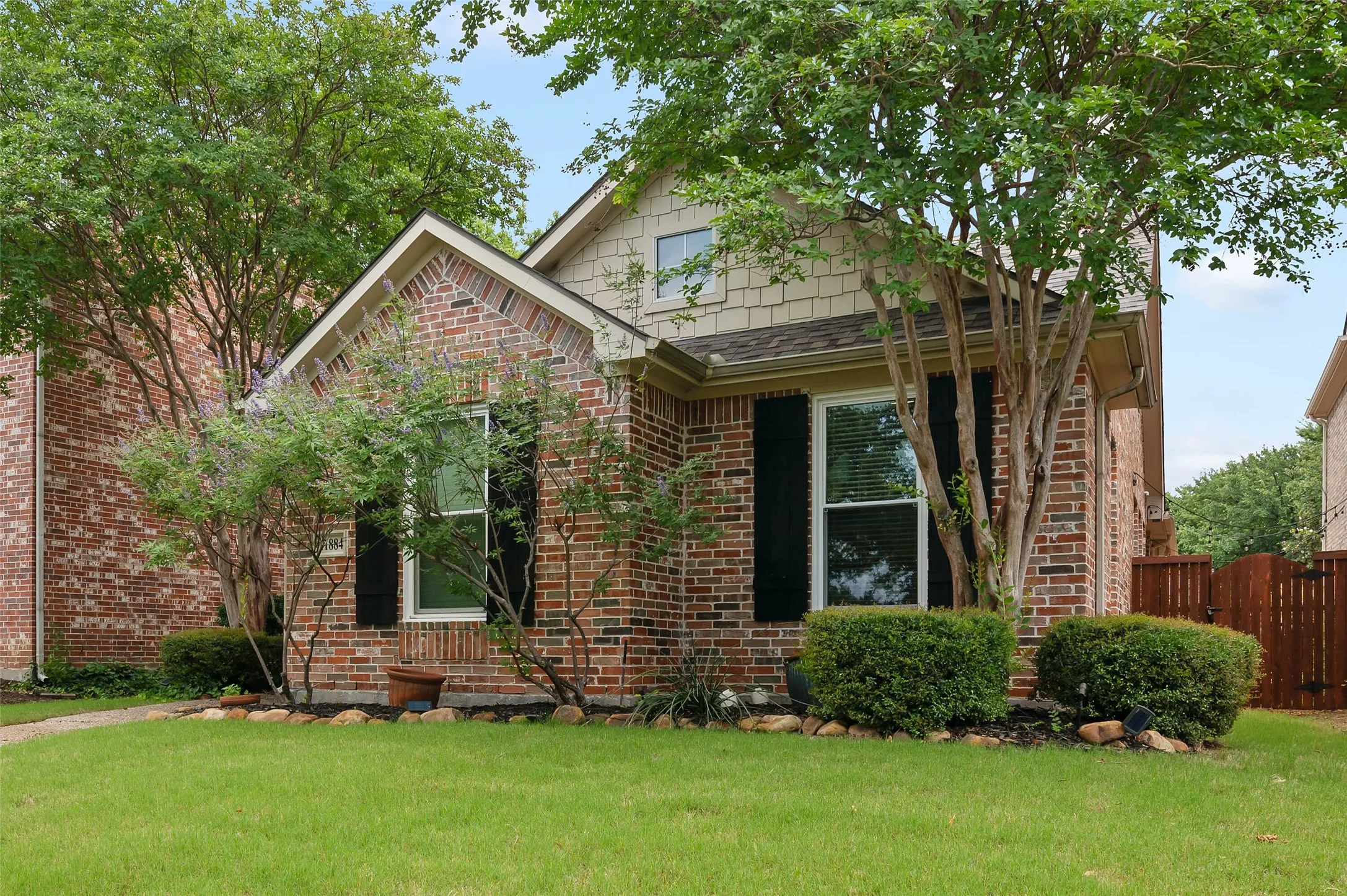 Brick facade residence featuring a prominent gable roofline and natural wood shingle accents