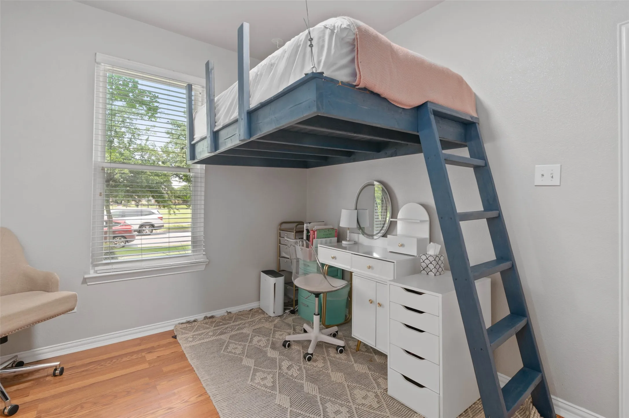 Room featuring a built-in loft bed with integrated ladder, wood-finish flooring, and a double-hung window with blinds