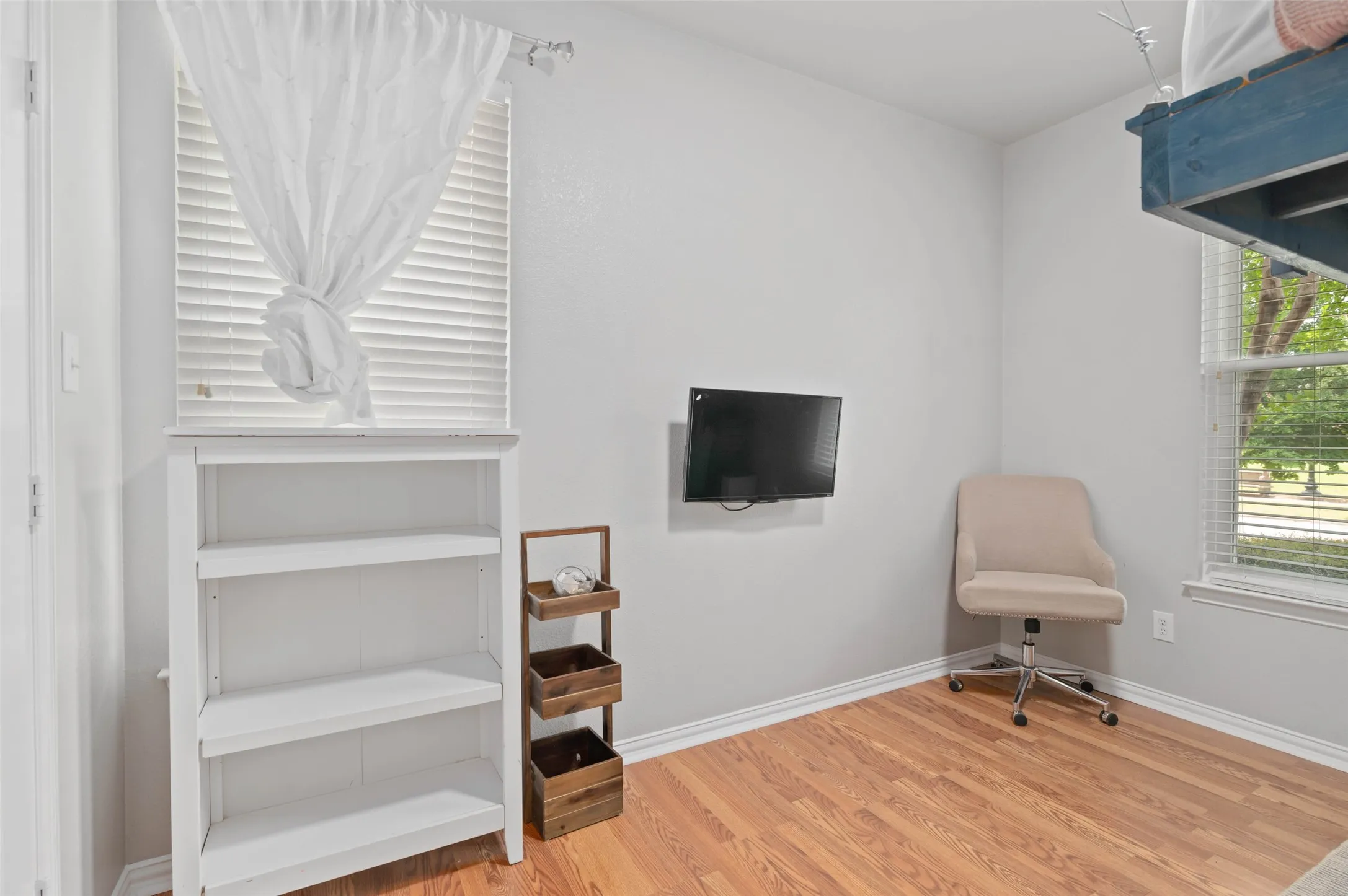Room featuring wood-finish flooring, a wall-mounted television, and a window with blinds