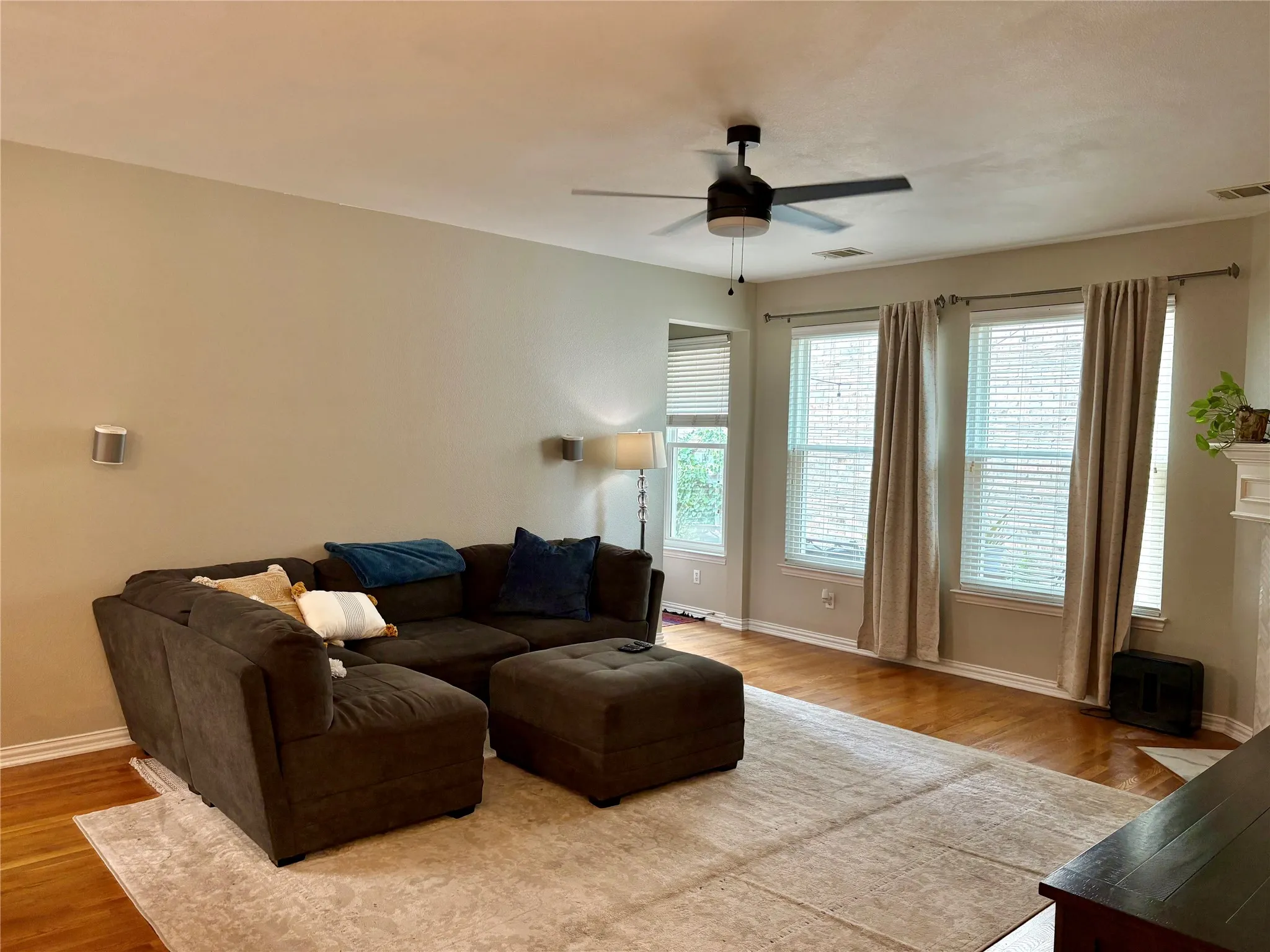 Hardwood-finish flooring, multiple windows with blinds, ceiling fan, and neutral wall tones