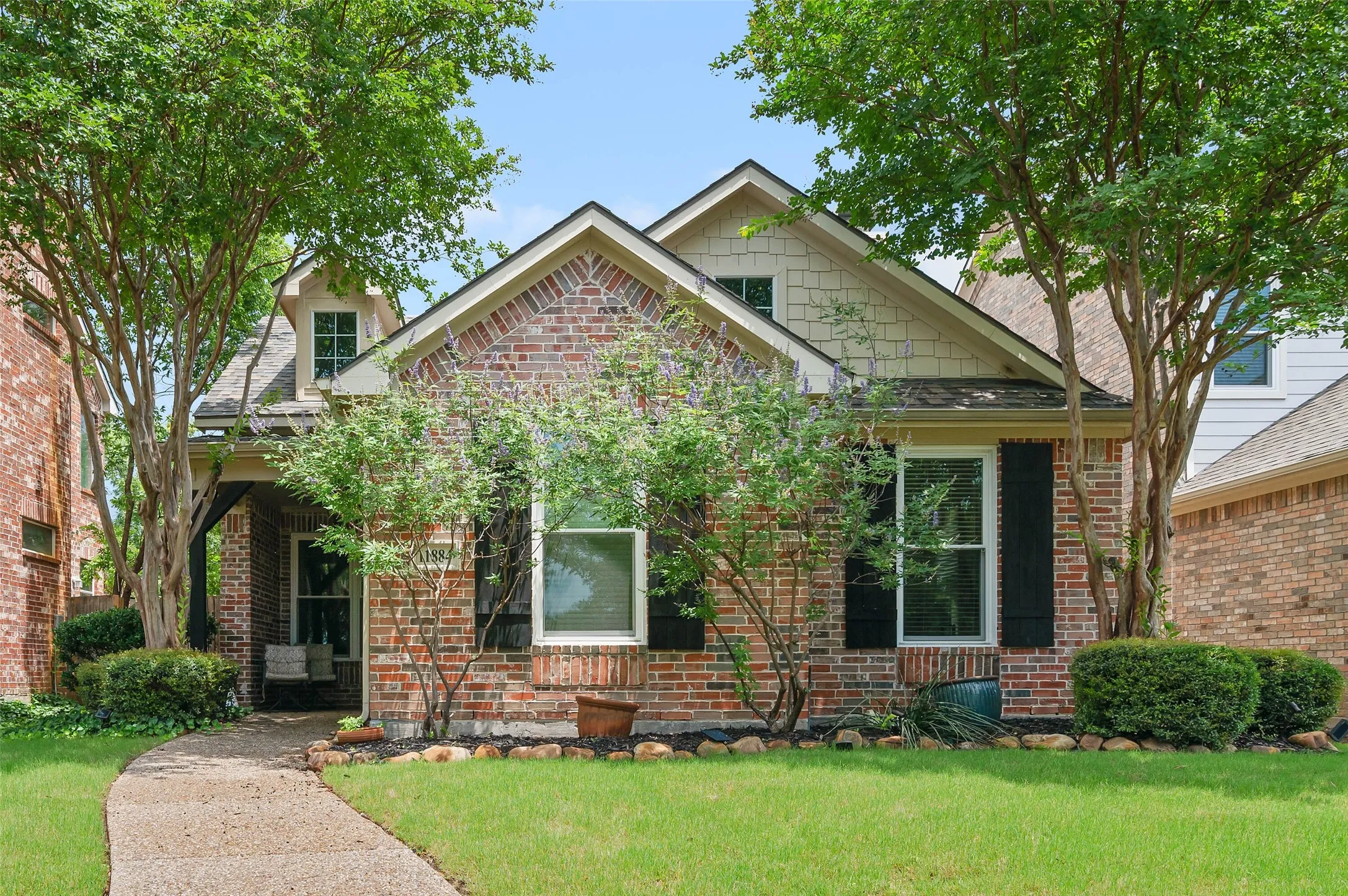 Brick facade residence featuring a covered front porch, dormer window, and black louvered shutters