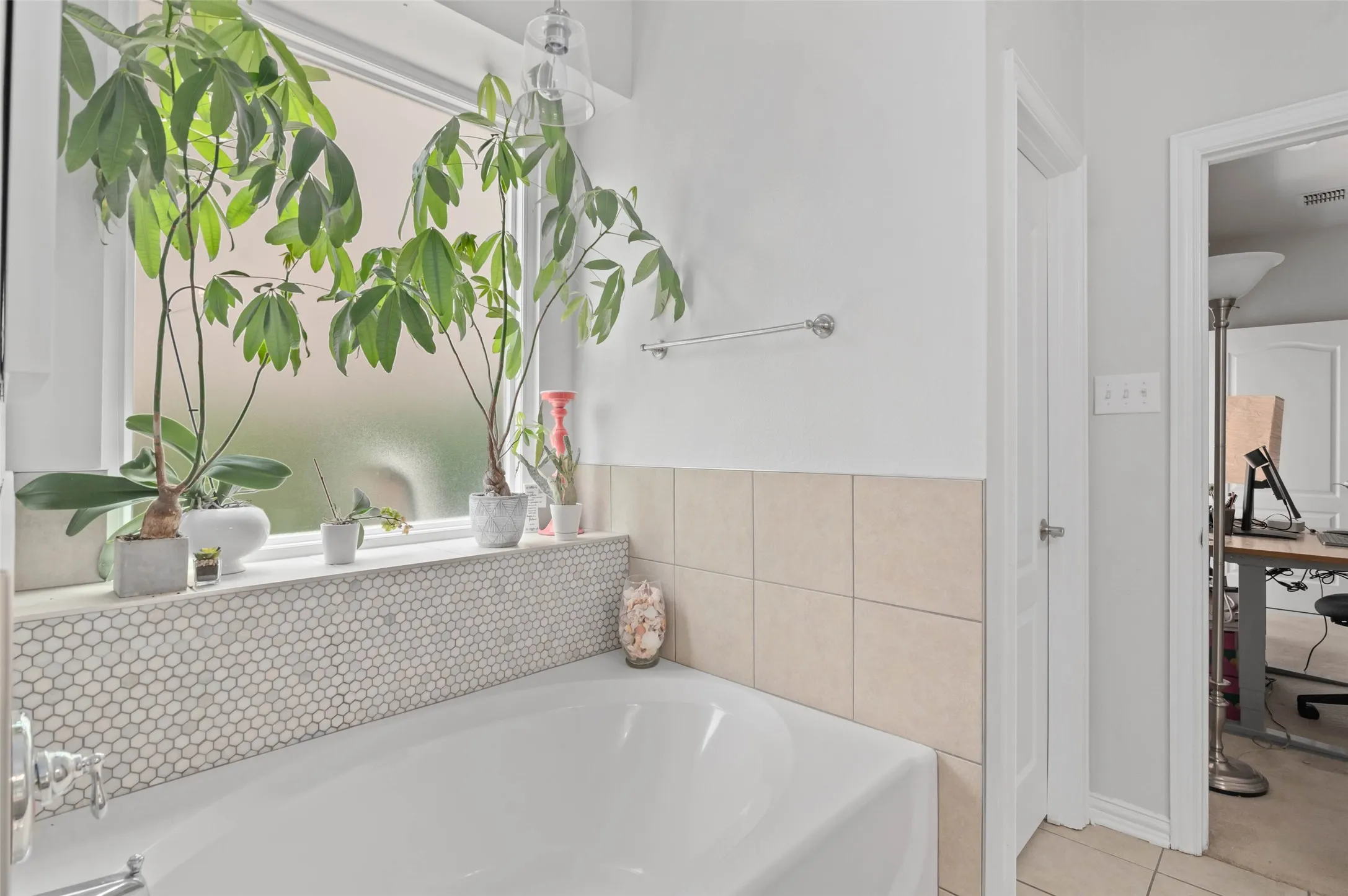 Soaking tub with a penny tile surround, frosted window, and chrome towel bar