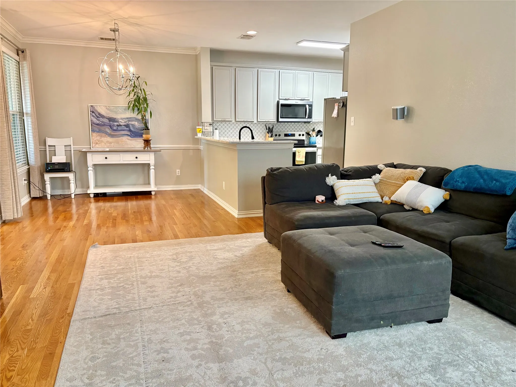 Hardwood flooring, crown molding, kitchen with light cabinetry, stainless steel appliances, and a built-in kitchen island