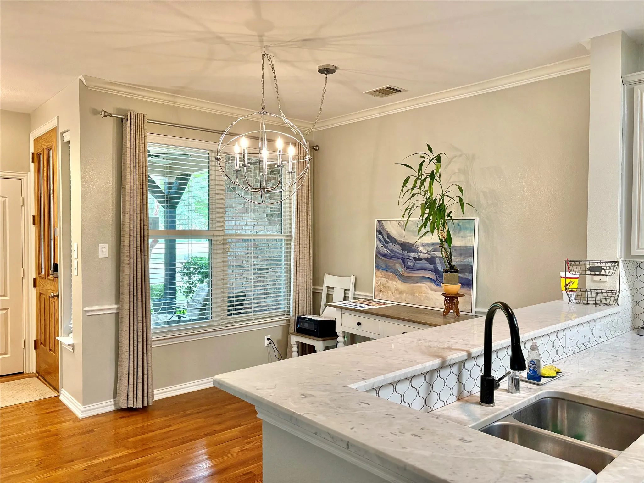 Hardwood flooring, crown molding, double-pane window, white countertop with honeycomb tile backsplash, and a double basin stainless steel sink with a black arched faucet