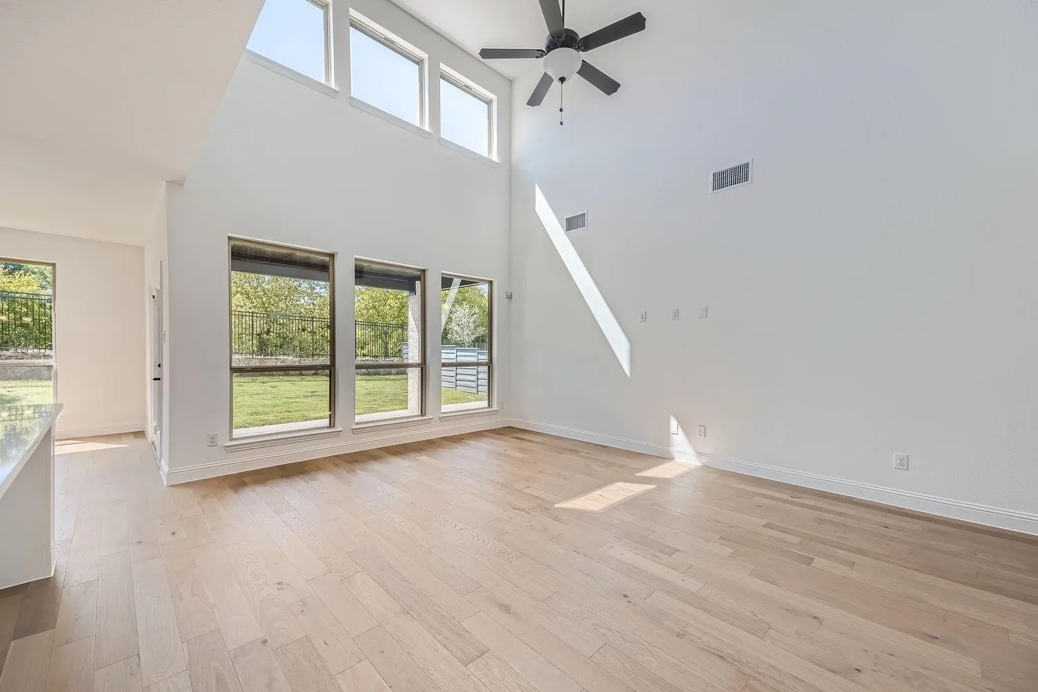 Vaulted ceilings with a ceiling fan, light wood-finish flooring, and multiple large windows with exterior green space