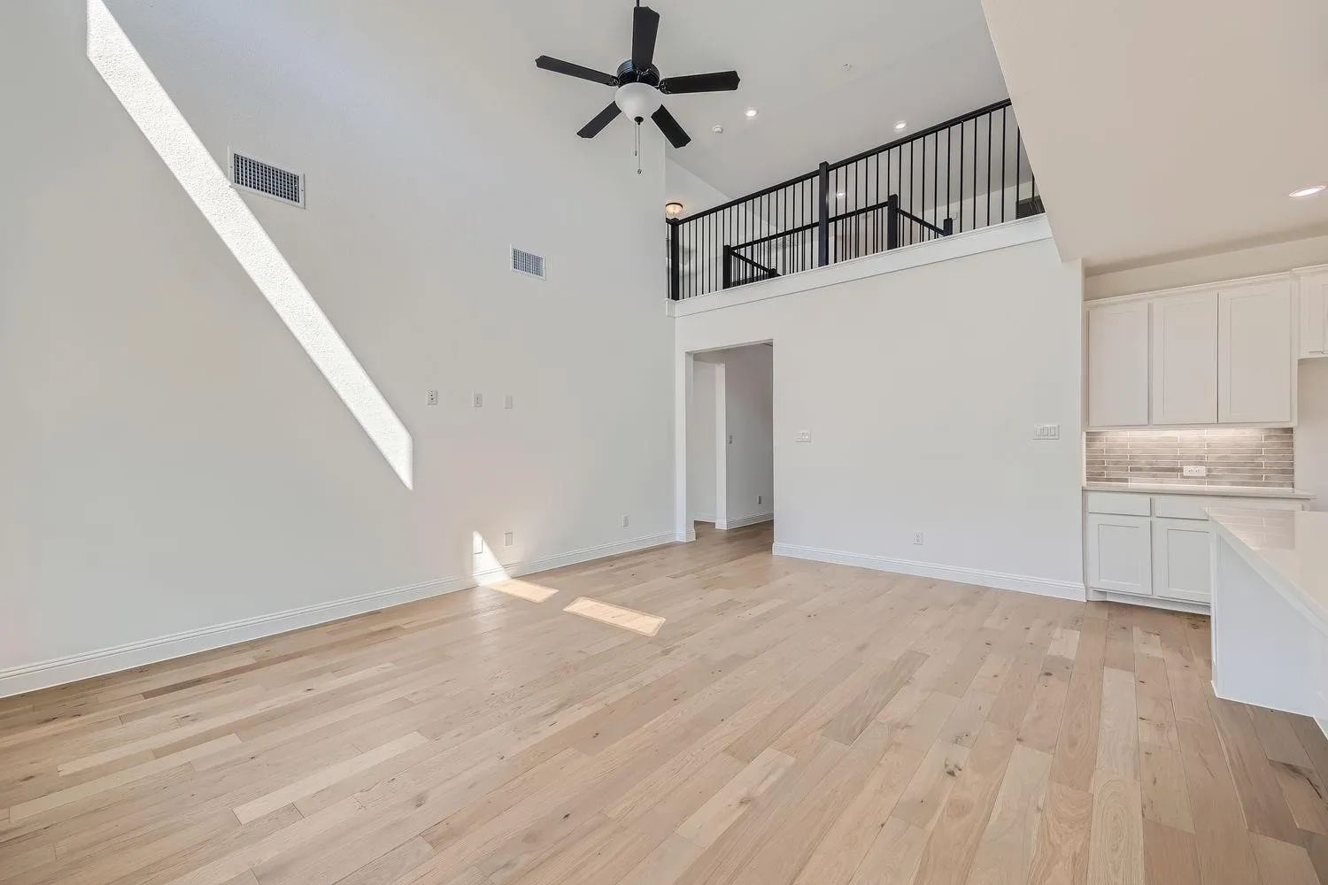 Open-concept living area featuring a vaulted ceiling with a ceiling fan, light wood-finish flooring, and a second-story loft with black iron railing