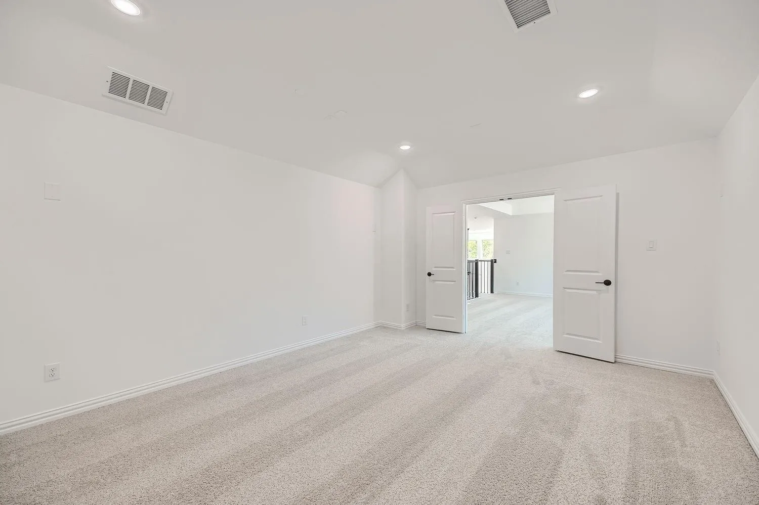 Spacious room featuring light-toned carpeting, crisp white walls, recessed ceiling lighting, and double-door entry