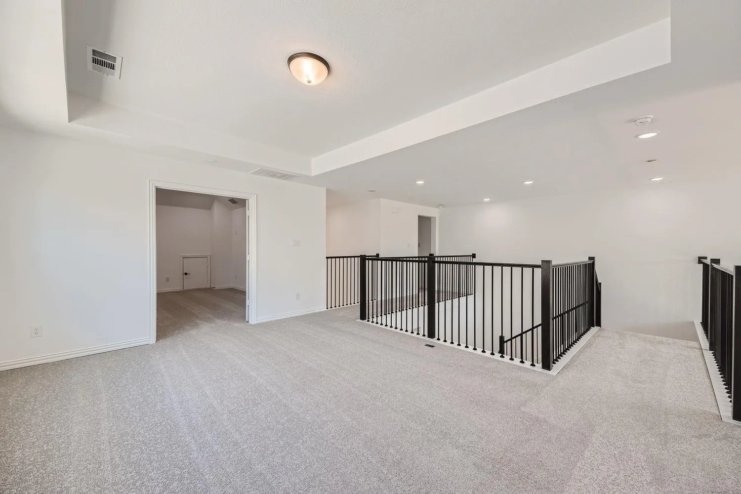 Expansive carpeted loft area featuring a tray ceiling, recessed lighting, and modern black balusters