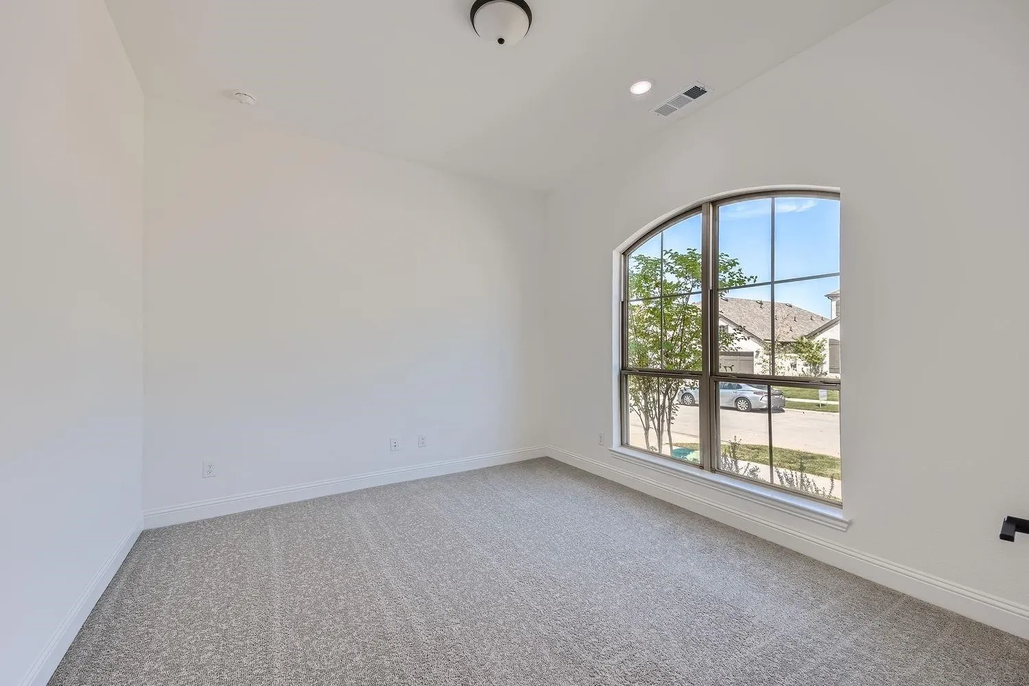 Arch-top window providing natural light, complemented by neutral-toned carpeting, white walls, and recessed lighting