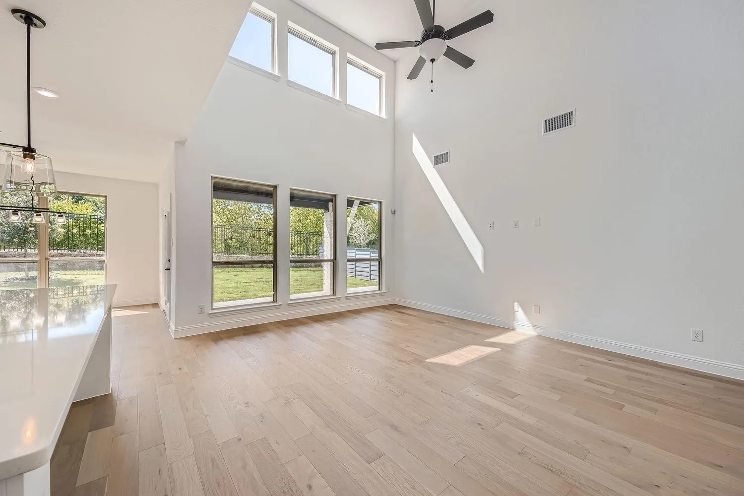 Spacious living area featuring a vaulted ceiling, wood-finish flooring, a contemporary ceiling fan, and multiple windows providing views of the exterior landscape