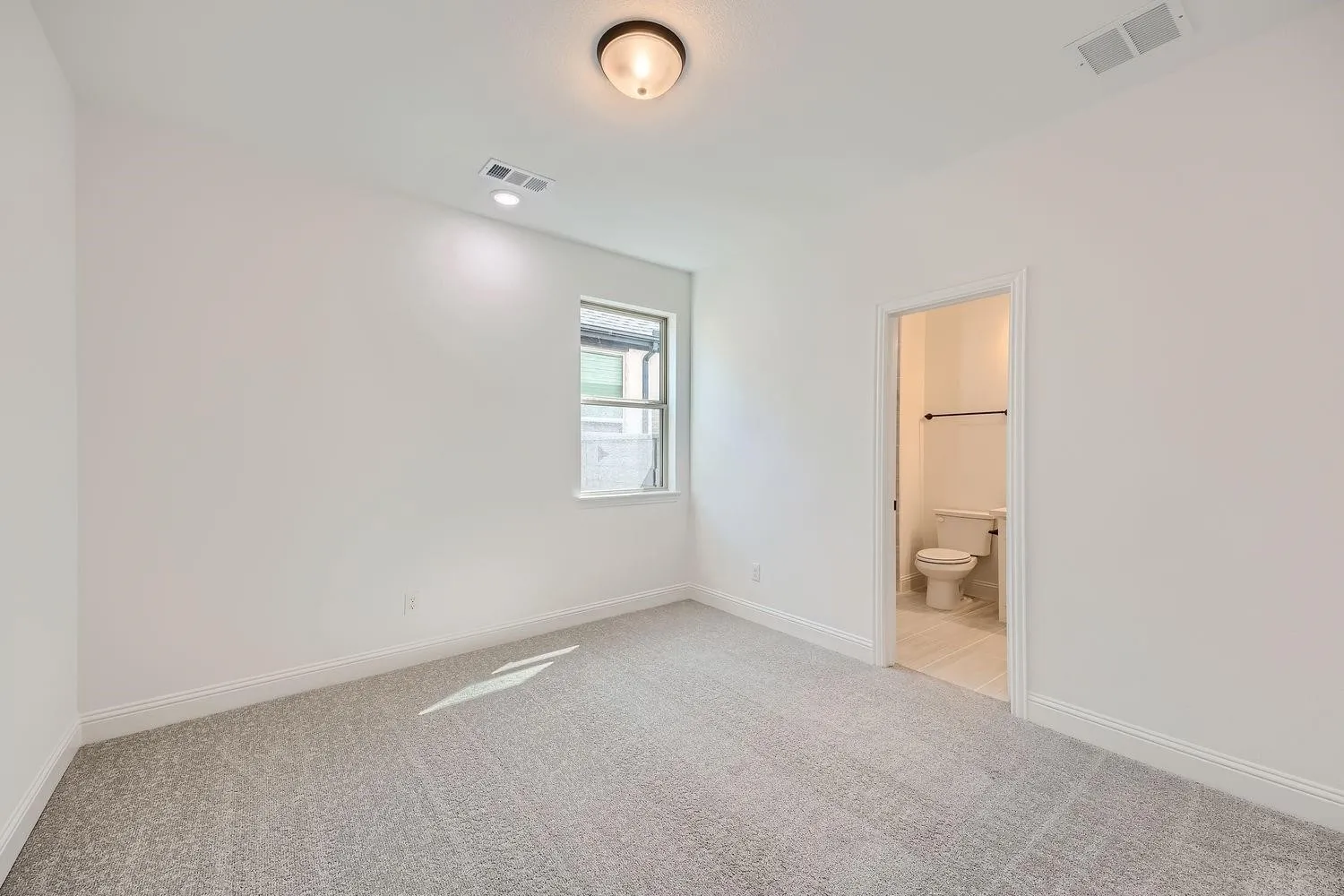 Carpeted room with a single window, recessed lighting, ceiling light fixture, and an attached bathroom featuring a toilet and towel rack