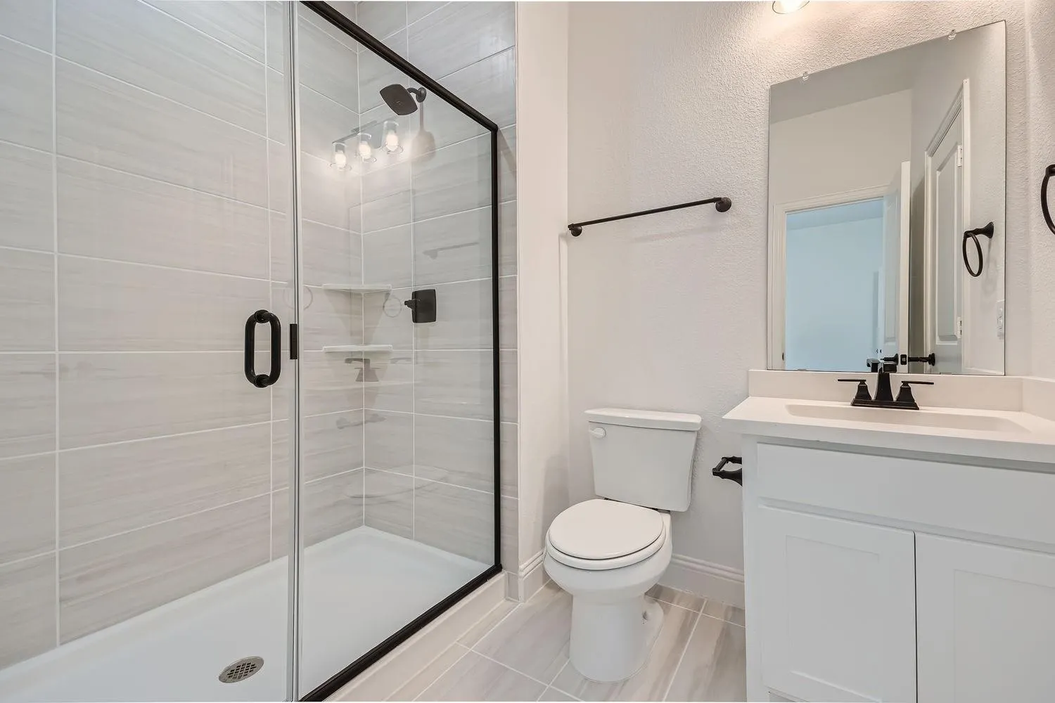 Bathroom featuring a glass-enclosed shower with matte black fixtures, light-toned rectangular wall tiling, and a white shower pan