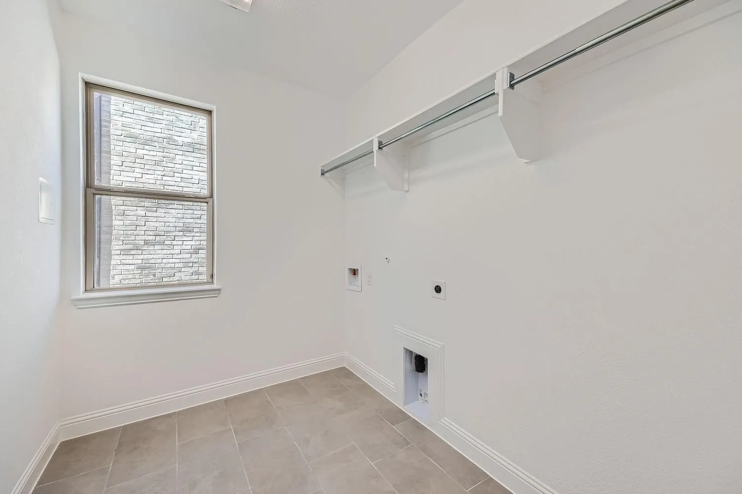 Utility room featuring tile flooring, a window with exterior brick detail, white baseboards, and a built-in hanging rod with shelving