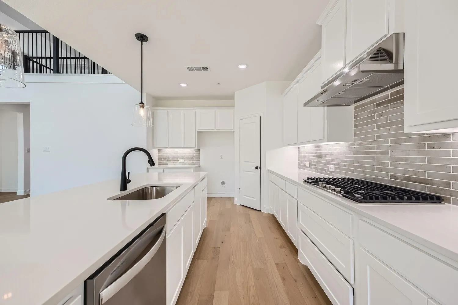 Modern kitchen featuring a large island with an undermount sink and a matte black faucet, stainless steel dishwasher, white cabinetry, and wood-finish flooring