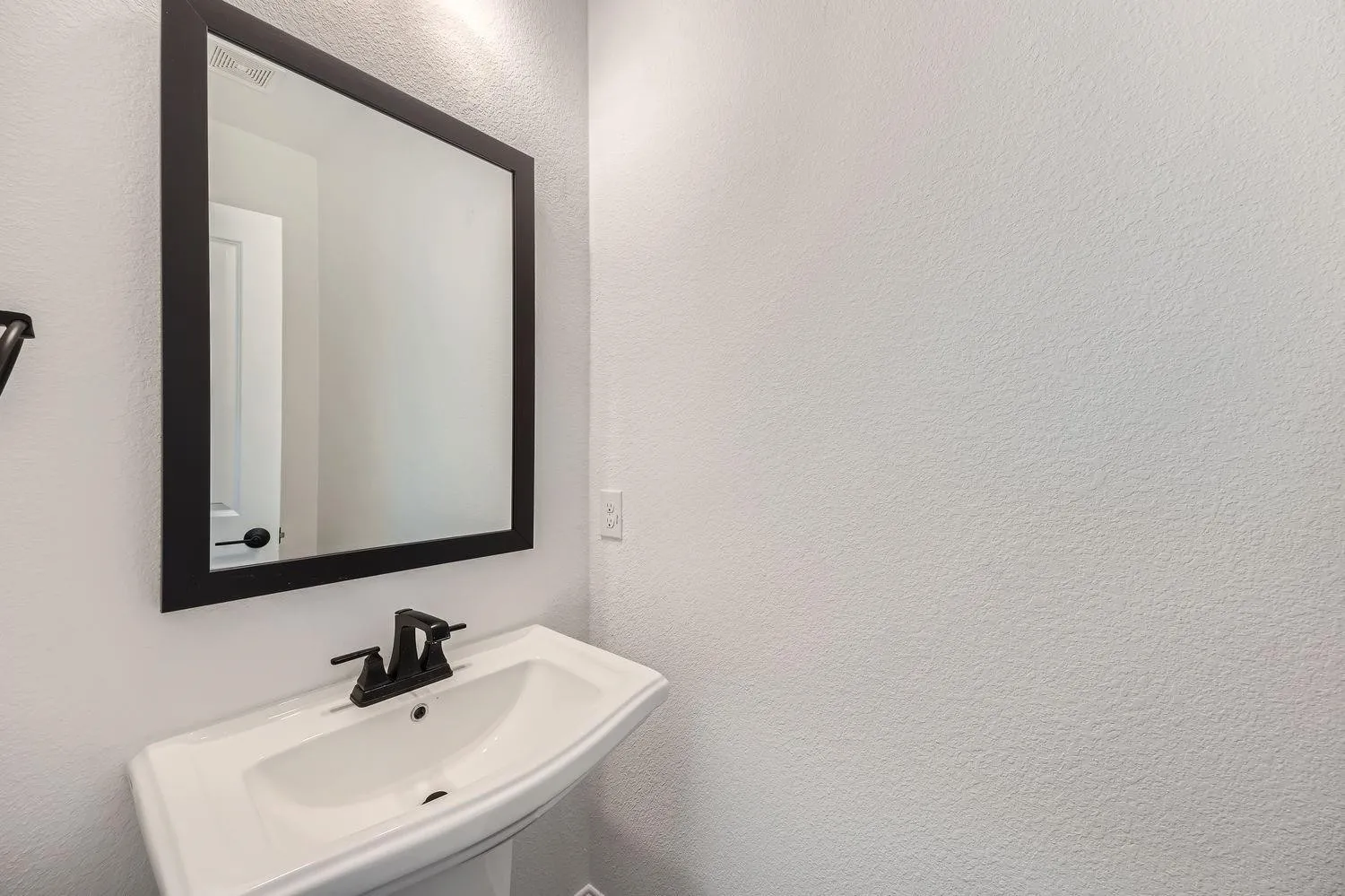 Pedestal sink with a matte black faucet and a framed wall mirror