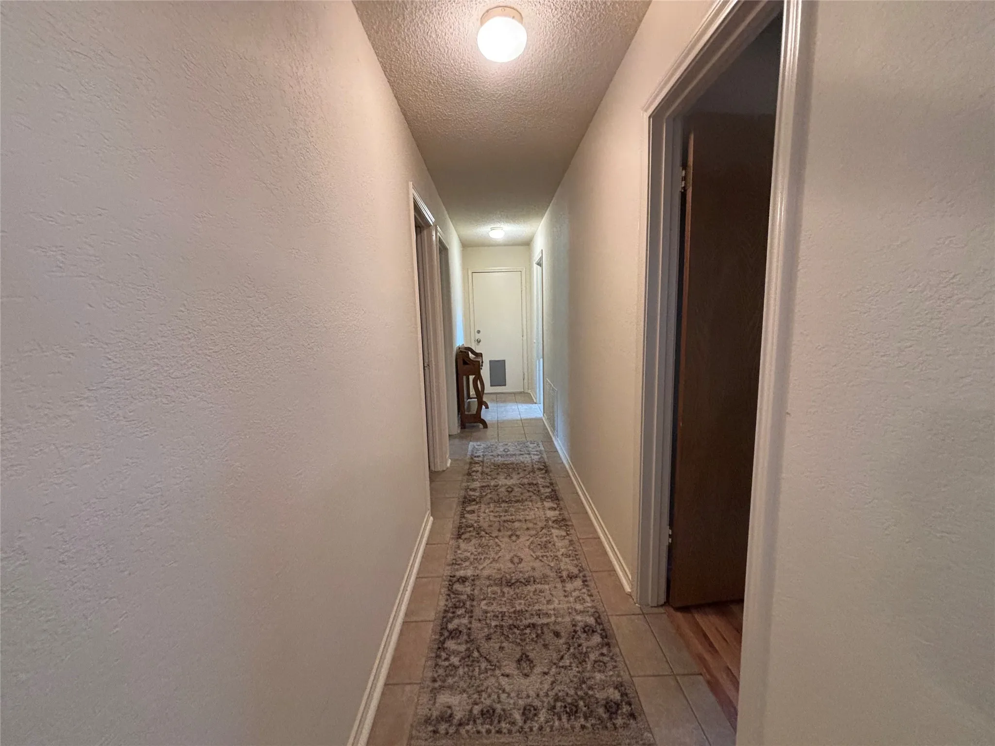 Hallway featuring tile flooring and light-toned walls leading to garage, bedrooms and secondary bath.