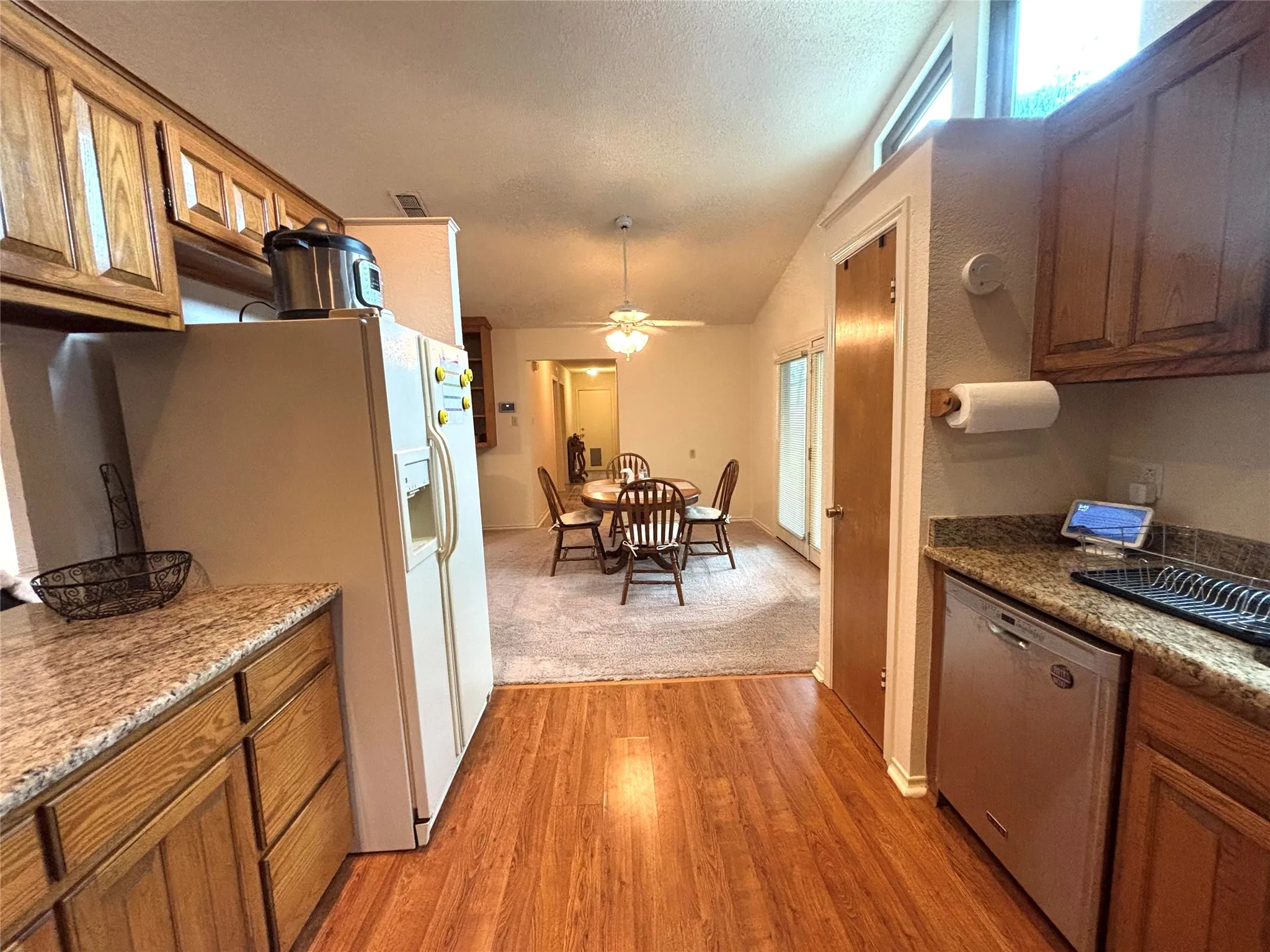 Kitchen featuring wood-finish flooring, wood cabinetry, stone-finish countertops, and a stainless steel dishwasher