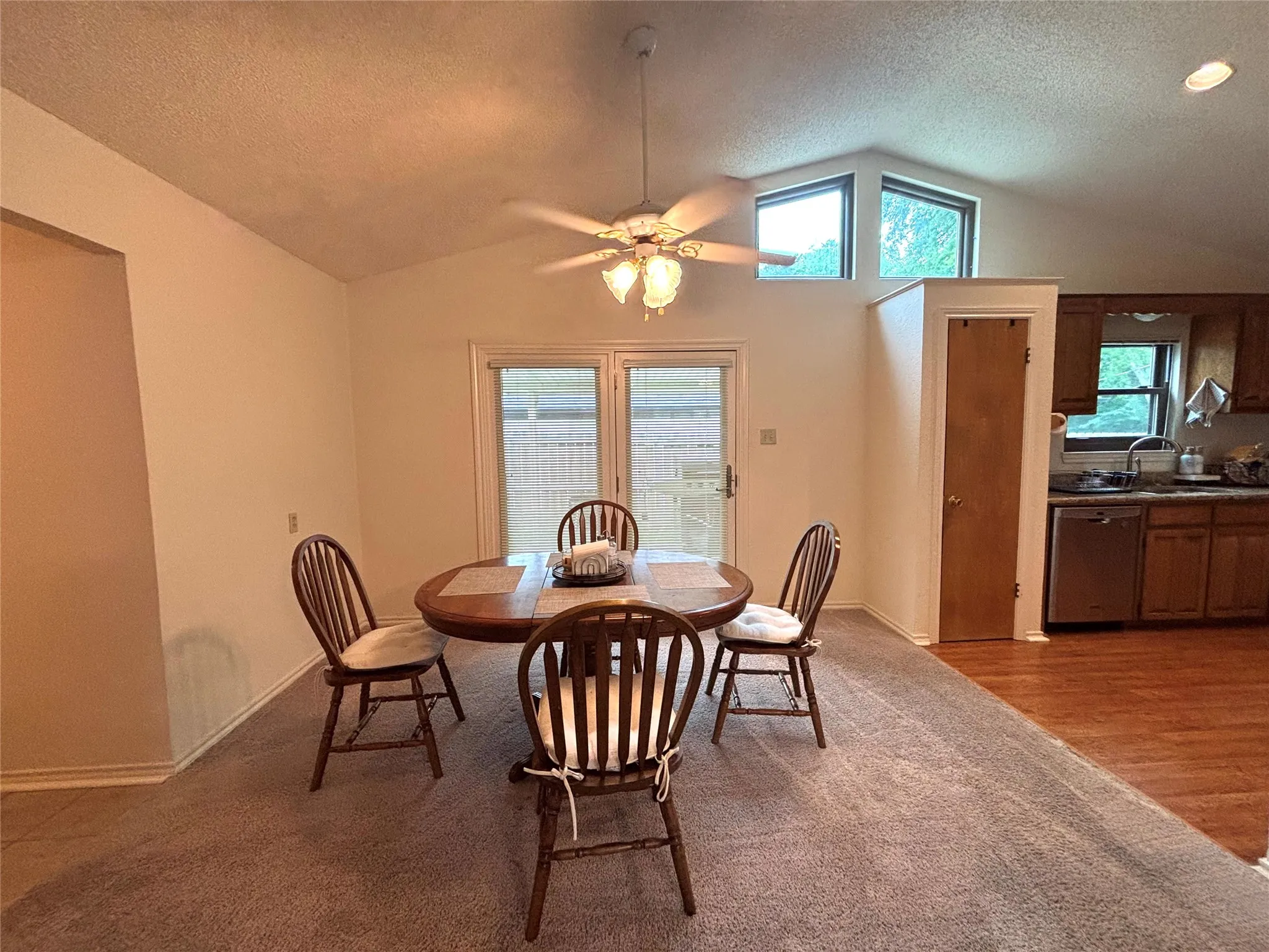 Vaulted ceiling dining area featuring high transom windows and a ceiling fan with light fixture