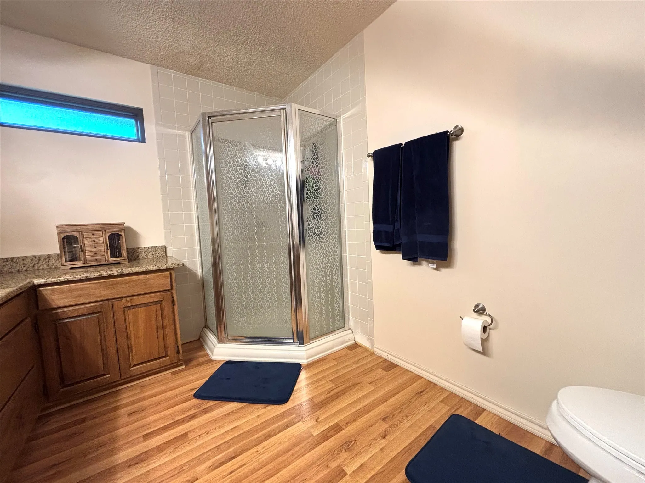 Corner glass-enclosed shower with textured privacy glass, complemented by a wood-finish flooring