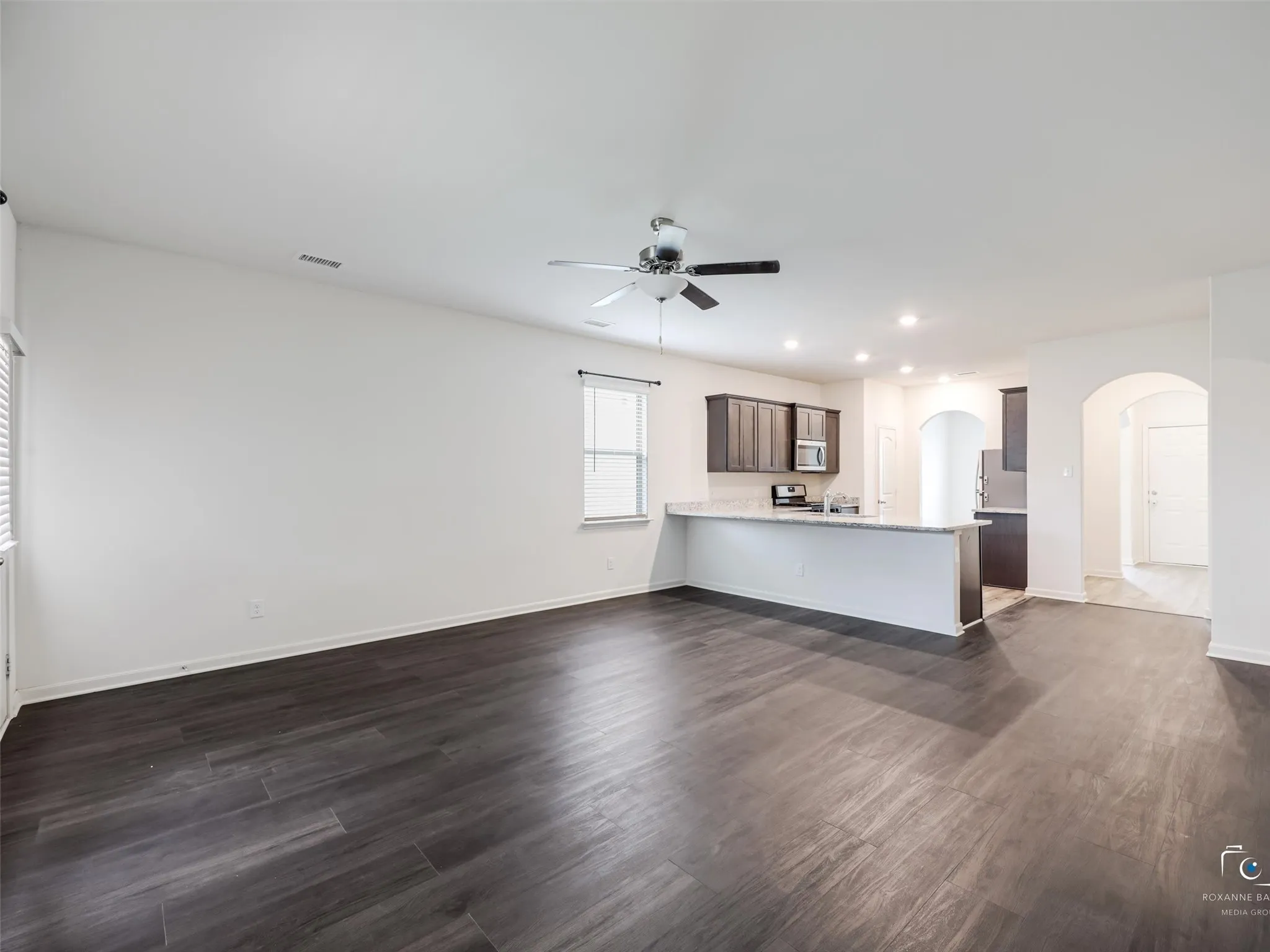 Expansive open-concept living area featuring wood-finish flooring, a ceiling fan, recessed lighting, and a kitchen with dark cabinetry and light-toned countertops