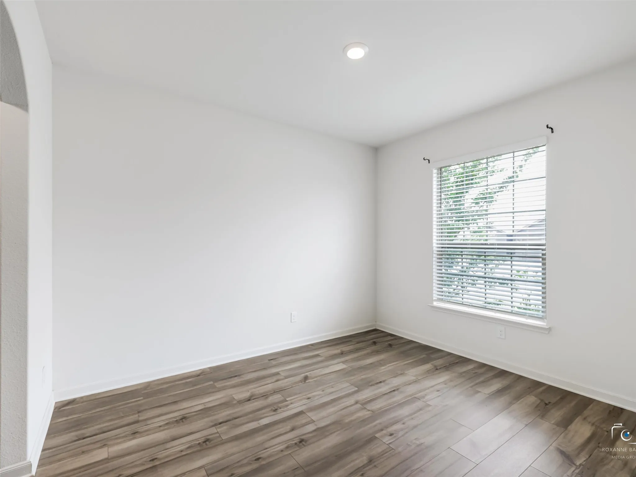 Recessed lighting illuminates the space, featuring wood-finish flooring, a window with horizontal blinds, and an arched entry