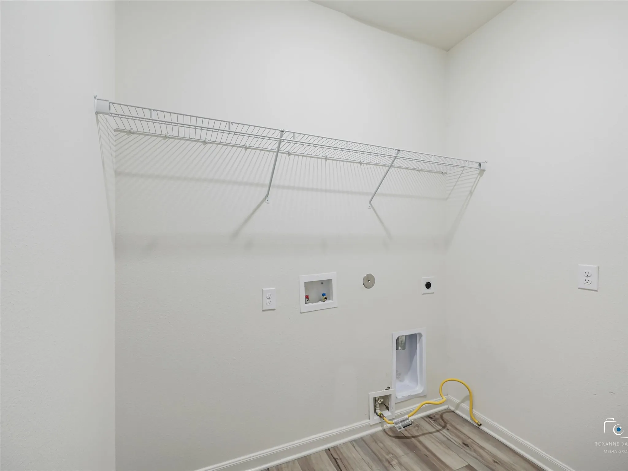 Laundry area featuring white wire shelving, utility hookups, and wood-finish flooring