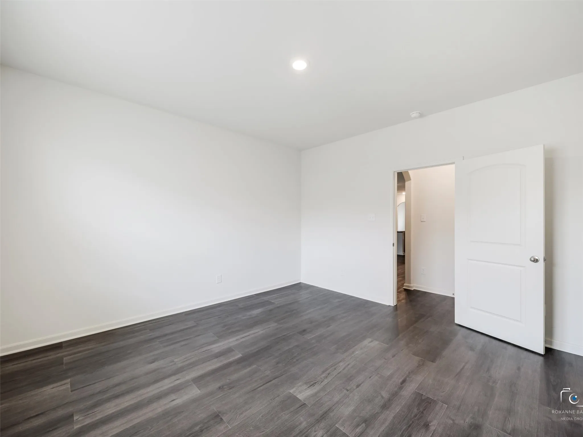 Wood-finish flooring with a cool-toned gray finish, recessed ceiling lighting, a white interior door with a rounded arch panel, and white walls