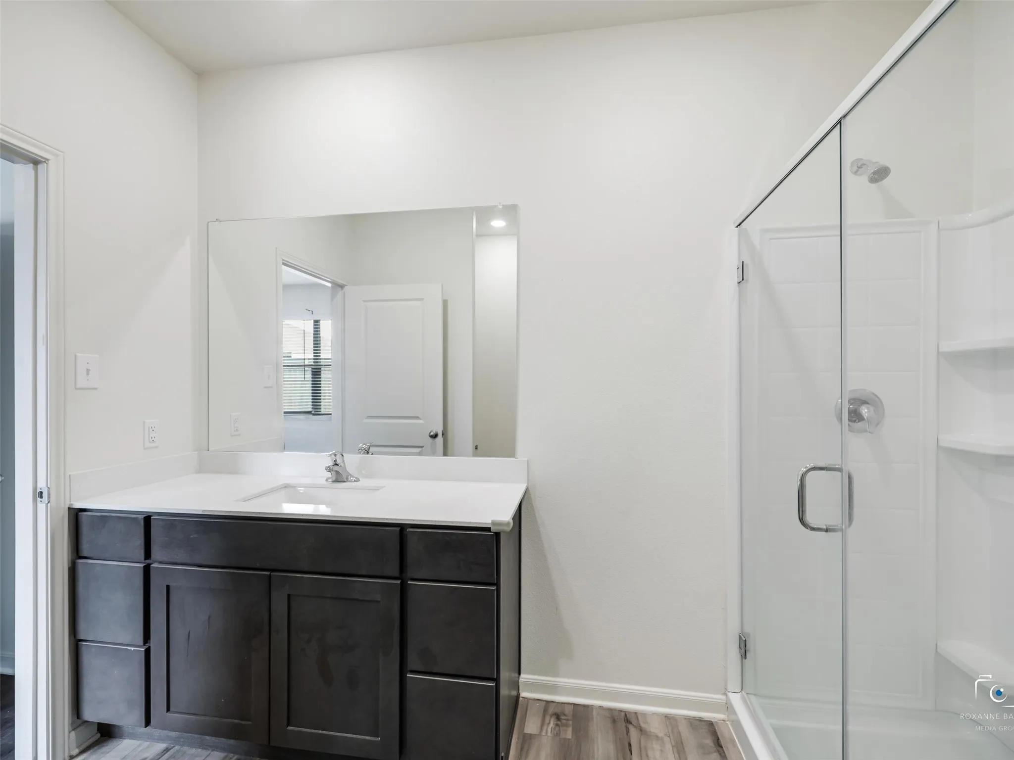 Bathroom featuring a dark wood-finish vanity with a white countertop, a large wall-mounted mirror, a glass-enclosed shower, and wood-finish flooring