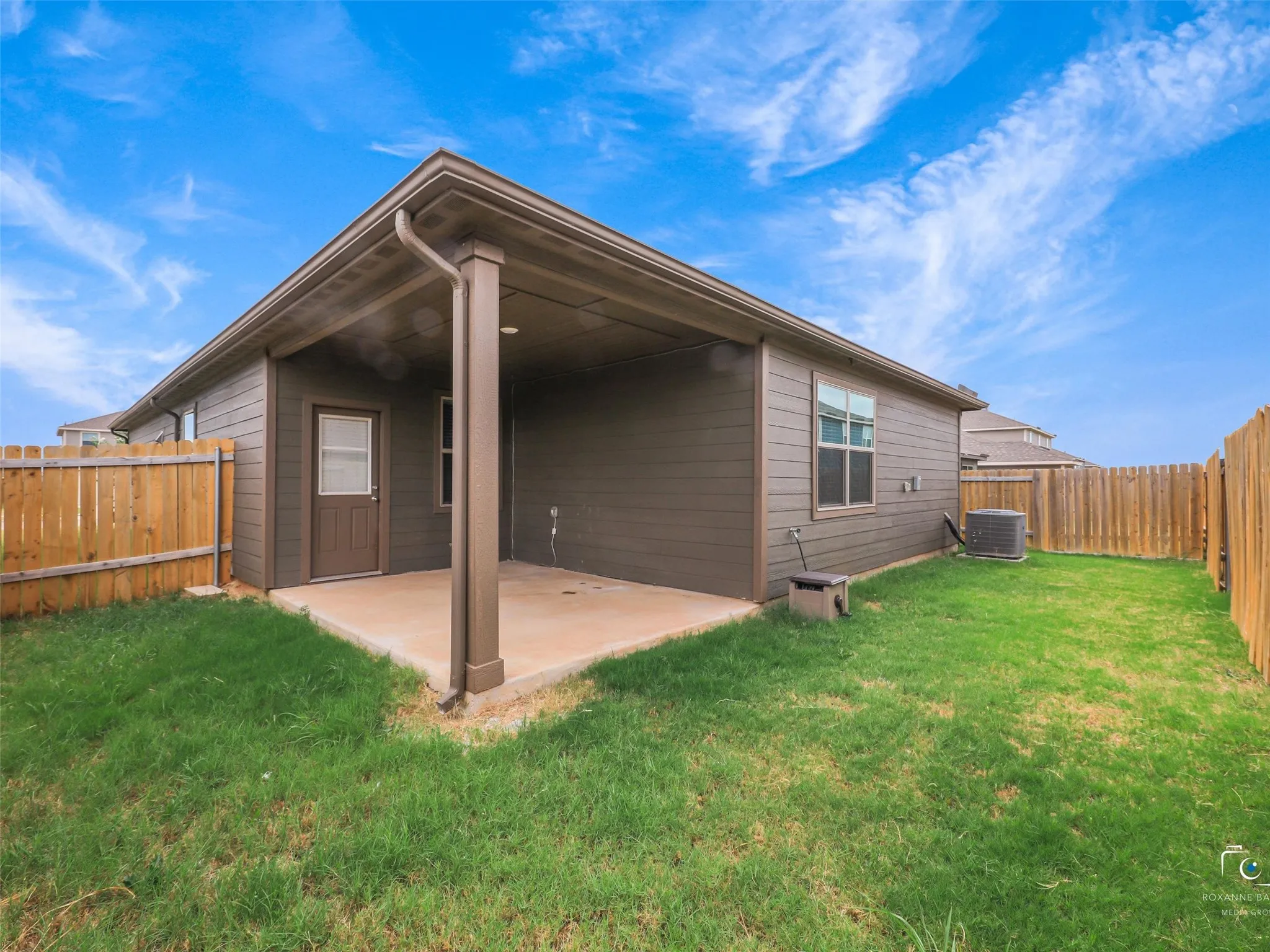 Covered concrete patio, wood privacy fencing, horizontal siding exterior, and a manicured lawn