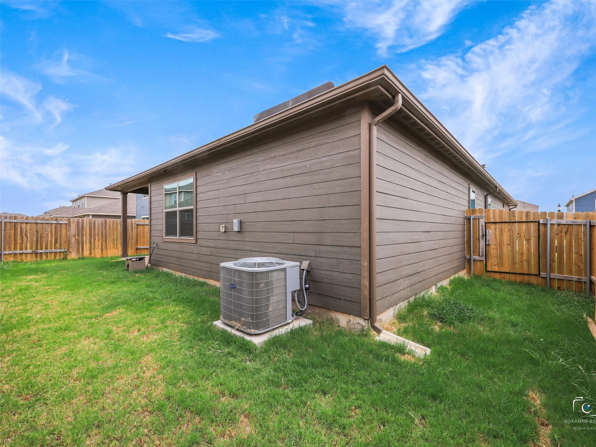 Expansive side yard featuring a grass lawn, wood plank siding, and a wooden privacy fence with gate