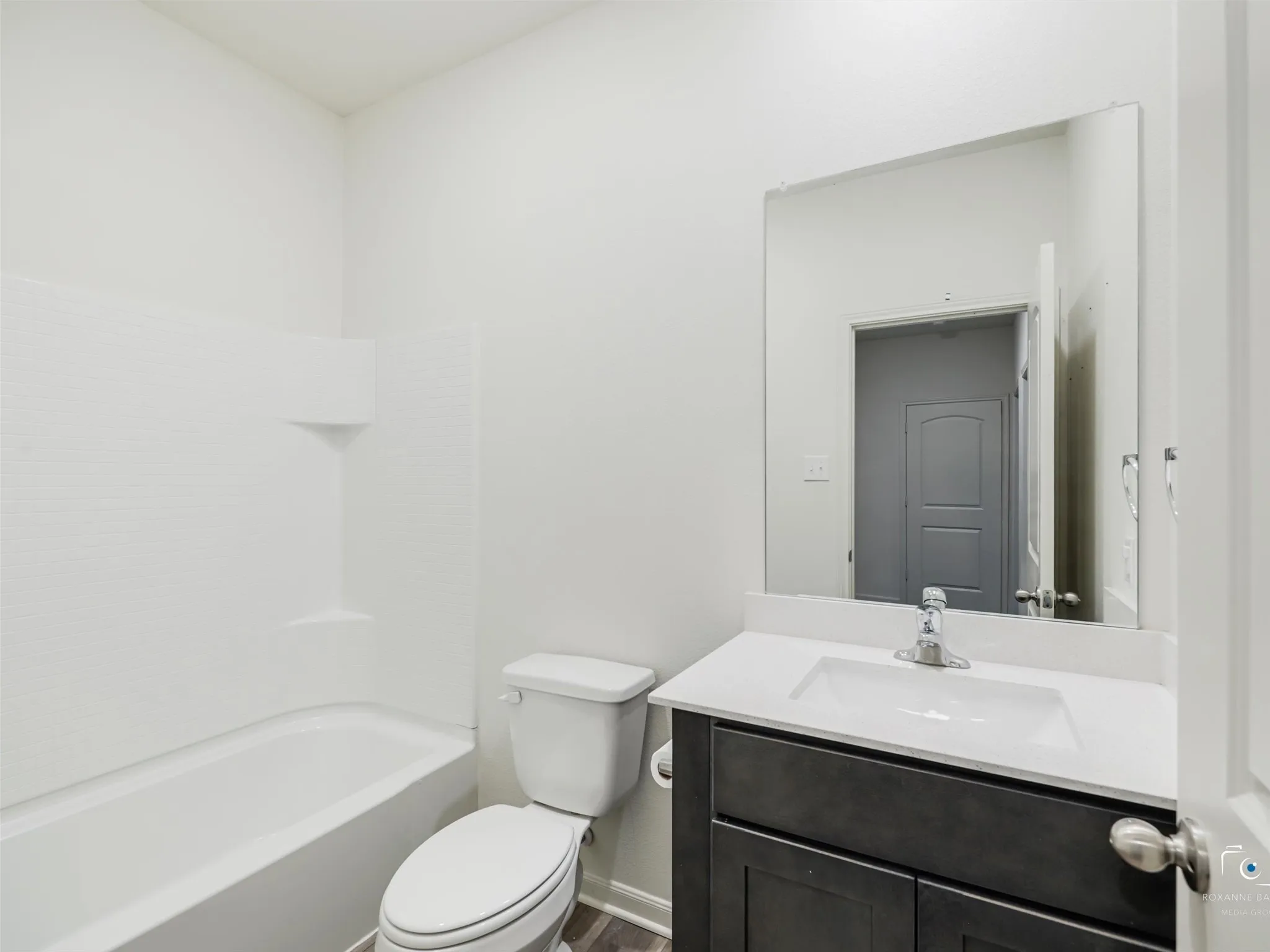 Full bathroom featuring a tub/shower combination, white toilet, and a vanity with a white countertop and dark cabinetry