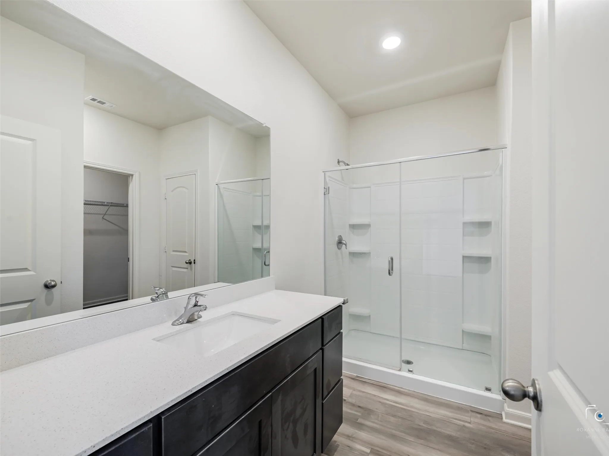 Spacious vanity with a white rectangular undermount sink, a large wall-mounted mirror, and a walk-in shower with clear glass enclosure