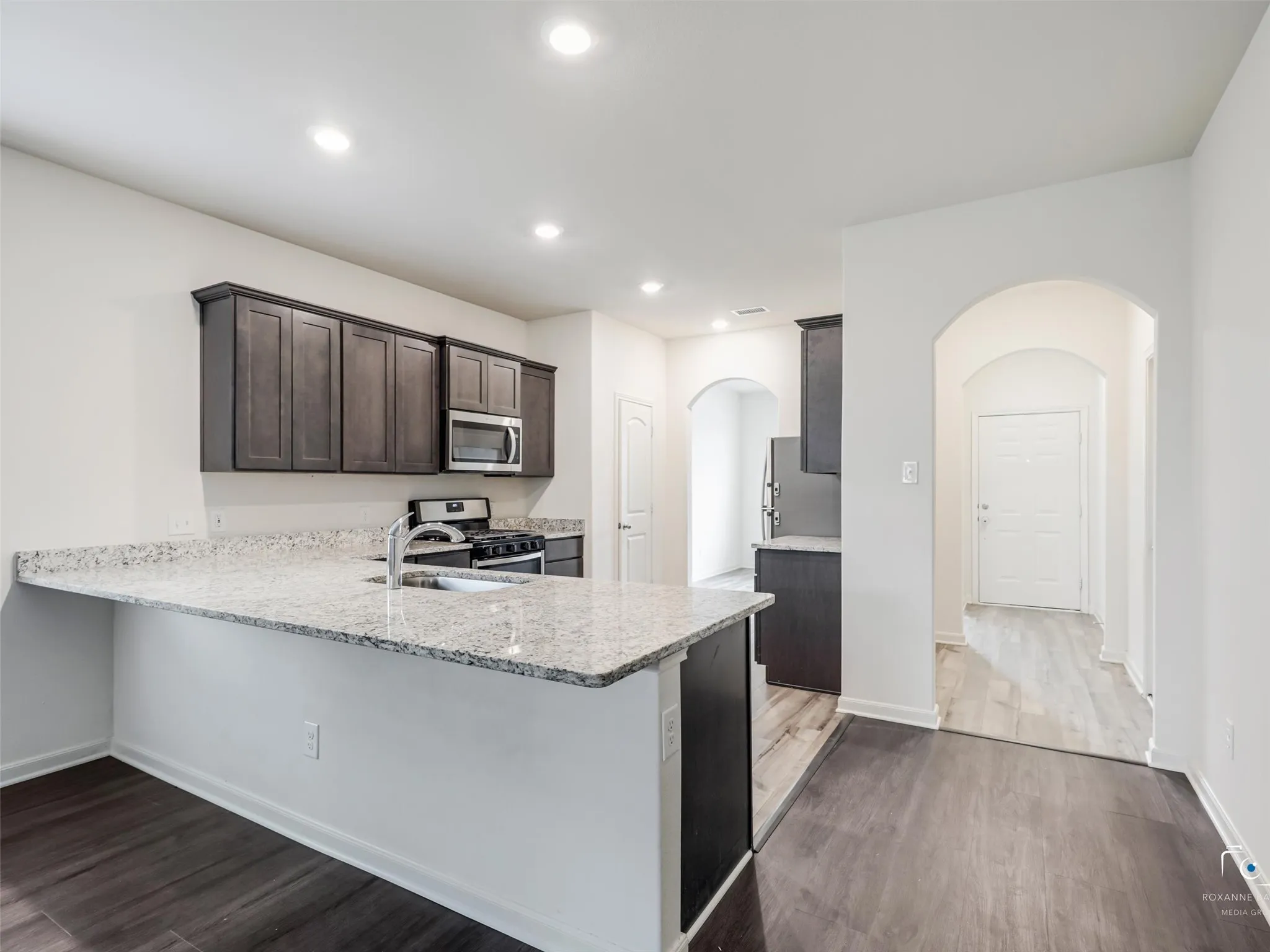 Kitchen featuring wood-finish flooring, granite countertops, recessed lighting, and dark wood cabinetry with stainless steel appliances