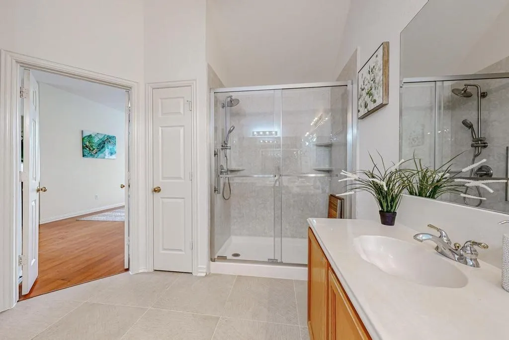 Bathroom featuring a glass-enclosed shower with tile surround, a single vanity with an undermount sink and light-toned countertop, wood-finish cabinetry, and light-toned floor tiling