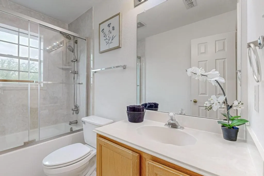 Bathroom featuring a shower-tub combination with glass enclosure, tiled surround, natural light from a double-hung window, a vanity with a light-colored countertop and wooden cabinetry, and a framed mirror