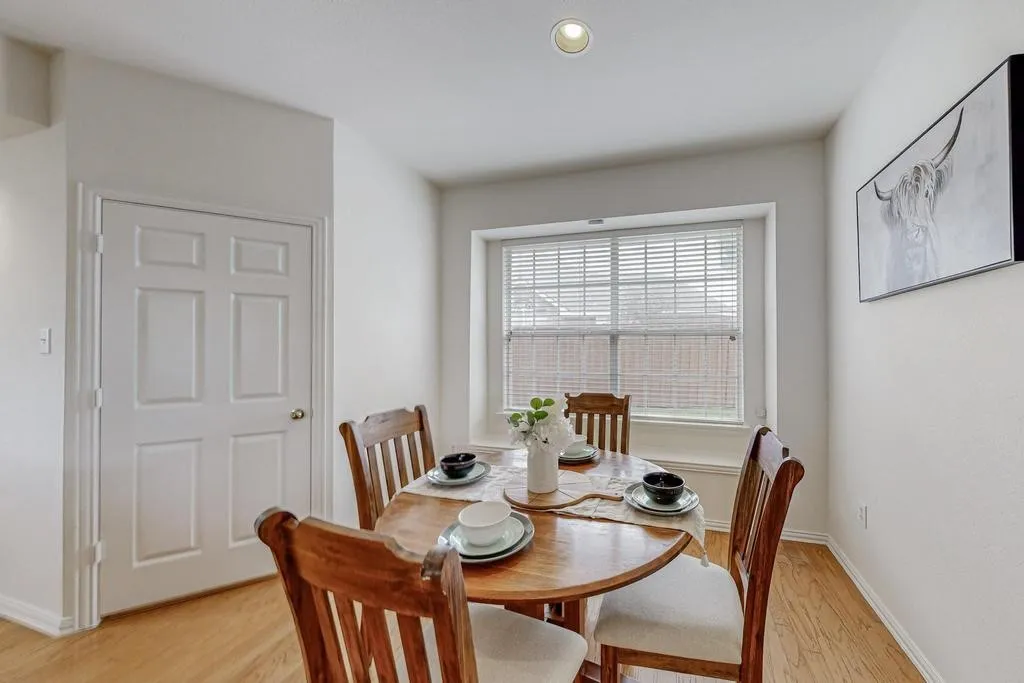 Bright dining area featuring wood-finish flooring, a multi-pane window with horizontal blinds, a six-panel interior door, and a recessed ceiling light fixture