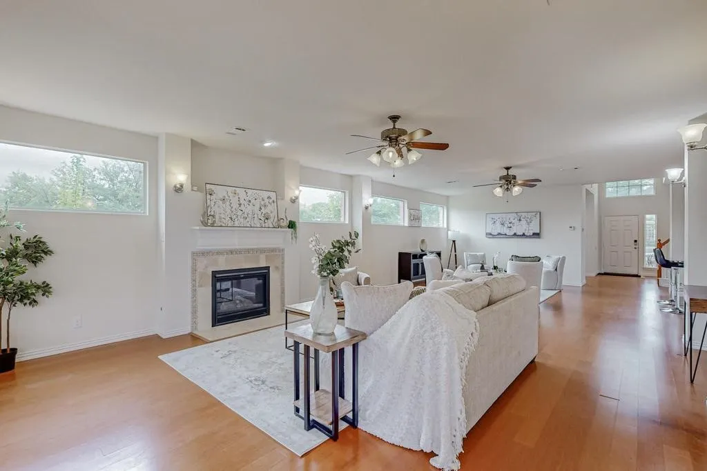Spacious living area featuring wood-finish flooring, a tiled fireplace with mantel, recessed lighting, and multiple ceiling fans