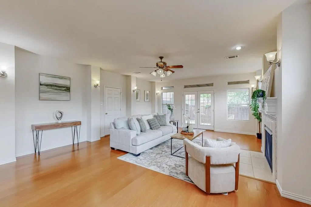 Expansive living area featuring warm wood-finish flooring, a ceiling fan, and a fireplace with a tiled surround
