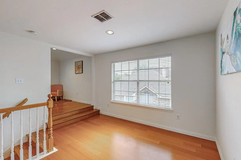 Interior space featuring wood-finish flooring, a staircase with wood newel posts and white spindles, and a window with horizontal blinds