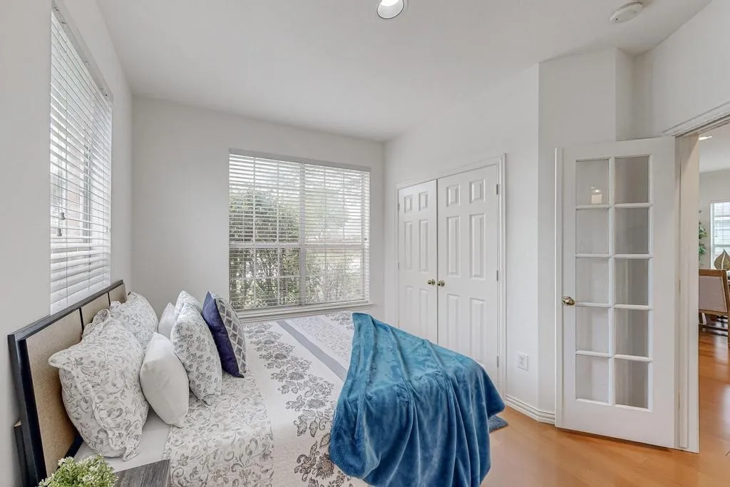Bright interior space with two windows featuring white blinds, recessed lighting, wood-finish flooring, a double-door closet, and a glass-paned interior door